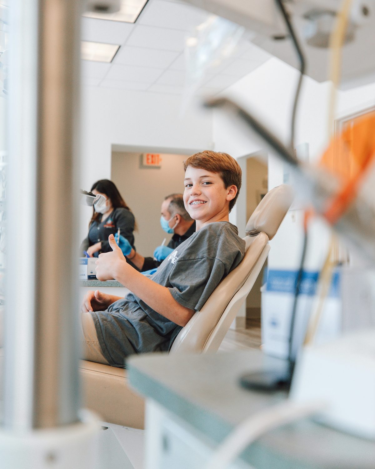 A smiling young patient giving a thumbs up in the dental chair